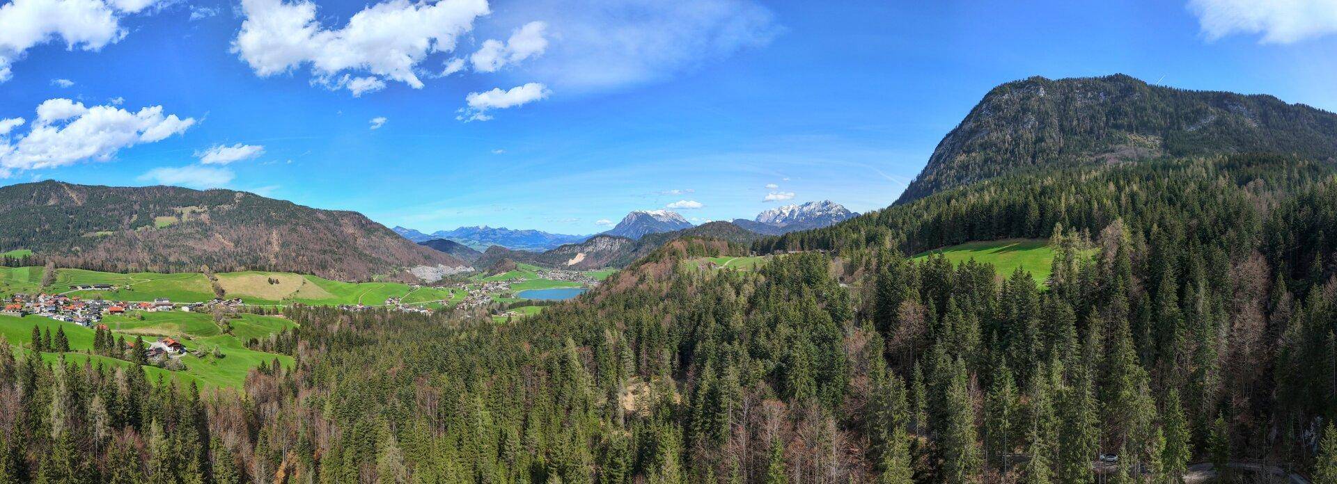 Malerisches Panorama mit grünen Wäldern, majestätischen Bergen und einem glitzernden See.