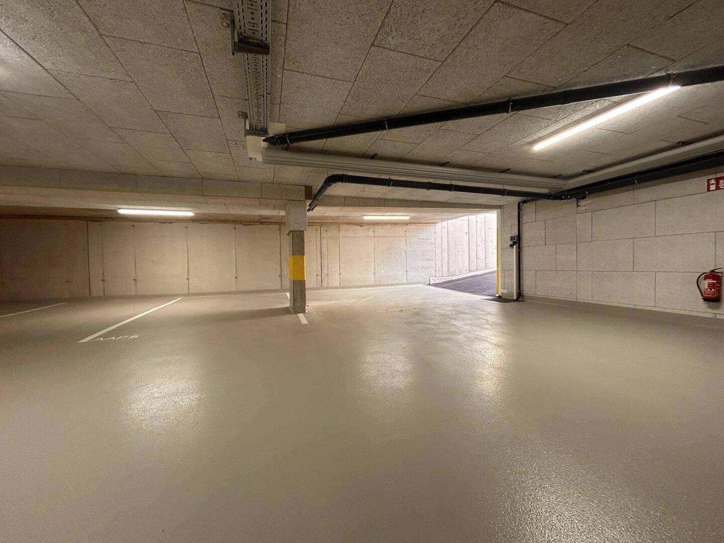 Geräumige Tiefgarage mit Betonwänden, Deckenplatten und einem Feuerlöscher an der Wand.
