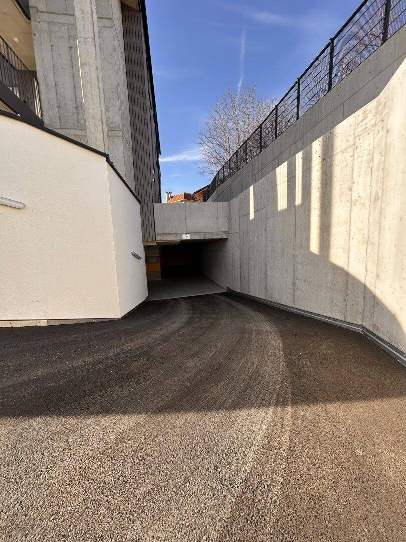 Geschwungene asphaltierte Zufahrt zur Tiefgarage, umgeben von hohen Betonmauern.