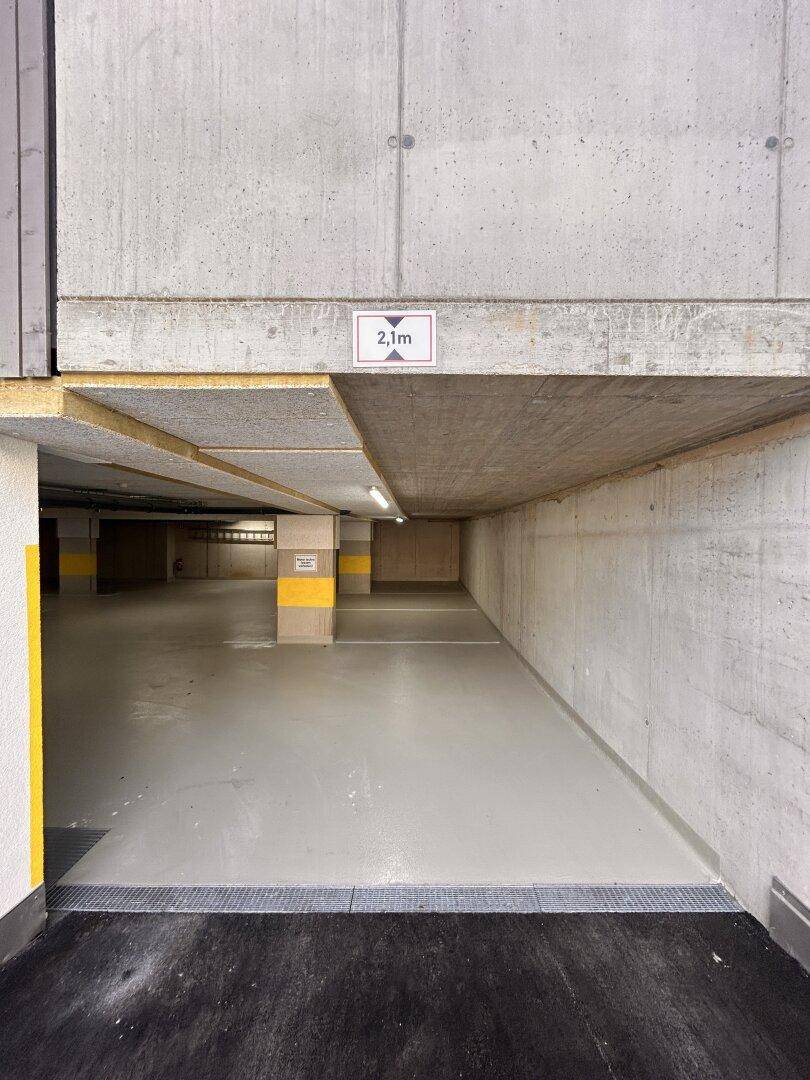 Einfahrt zur Tiefgarage mit Höhenbegrenzung von 2,1 Metern und sichtbaren Betonstrukturen.