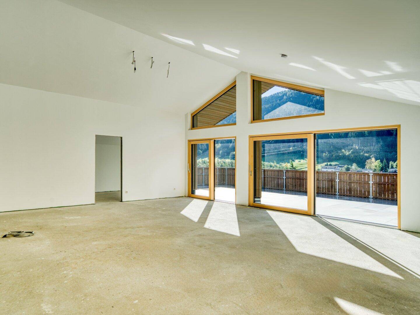Heller, leerer Wohnraum mit großen Schiebetüren, Bergblick und schrägen Decken, bereit für den Ausbau.