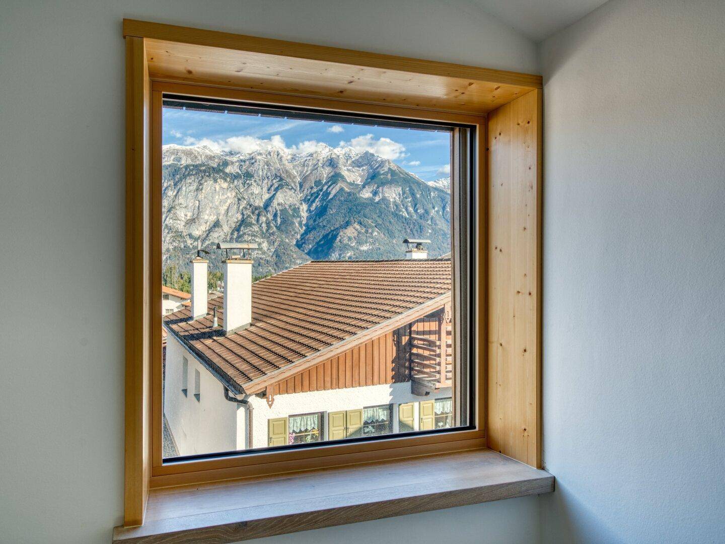 Fenster mit Holzrahmen bietet einen atemberaubenden Blick auf schneebedeckte Berge und Dächer.