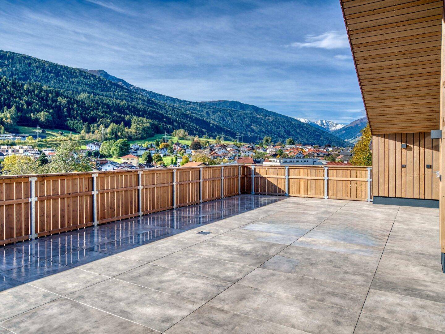 Weitläufige Terrasse mit Fliesenboden und Holzzaun, bietet einen Panoramablick auf das Tal und die Berge.