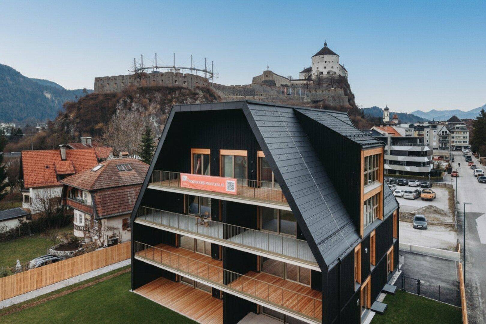 Detailansicht des modernen Gebäudes mit schwarzer Fassade, Holzverkleidung und mehreren Balkonen.