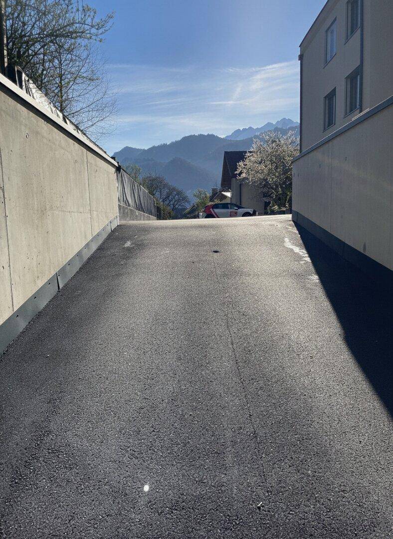 Asphaltierte Auffahrt mit Betonwänden und Blick auf die Berge im Hintergrund.