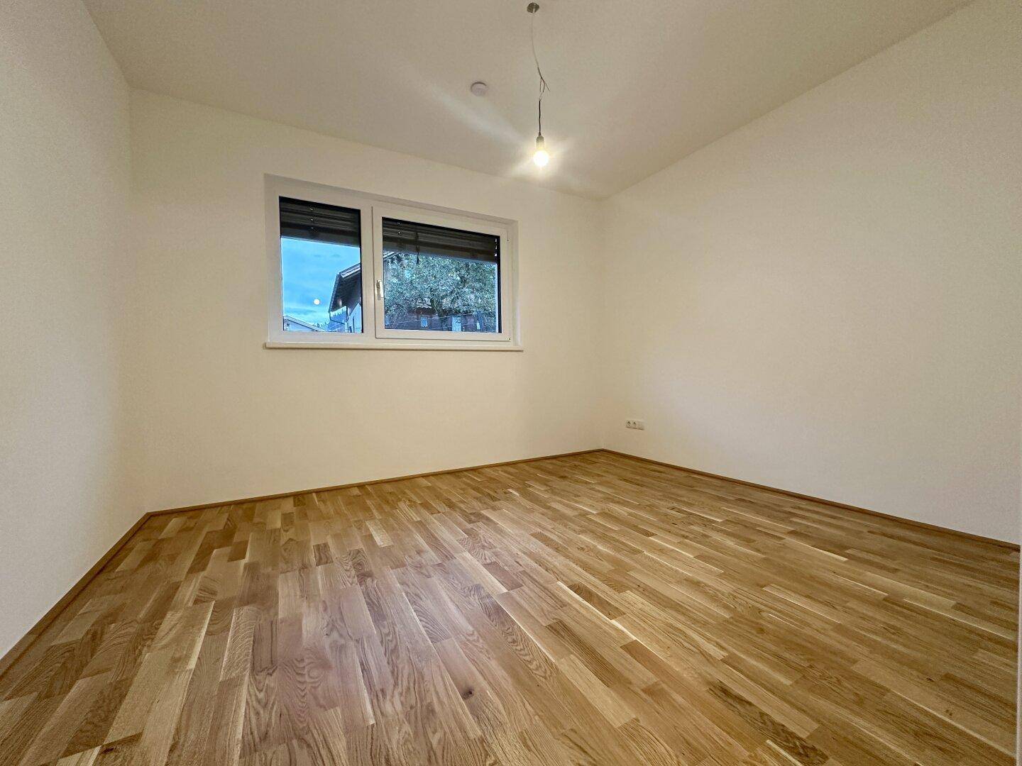 Helles Schlafzimmer mit Parkettboden und großem Fenster, bereit zur individuellen Gestaltung.