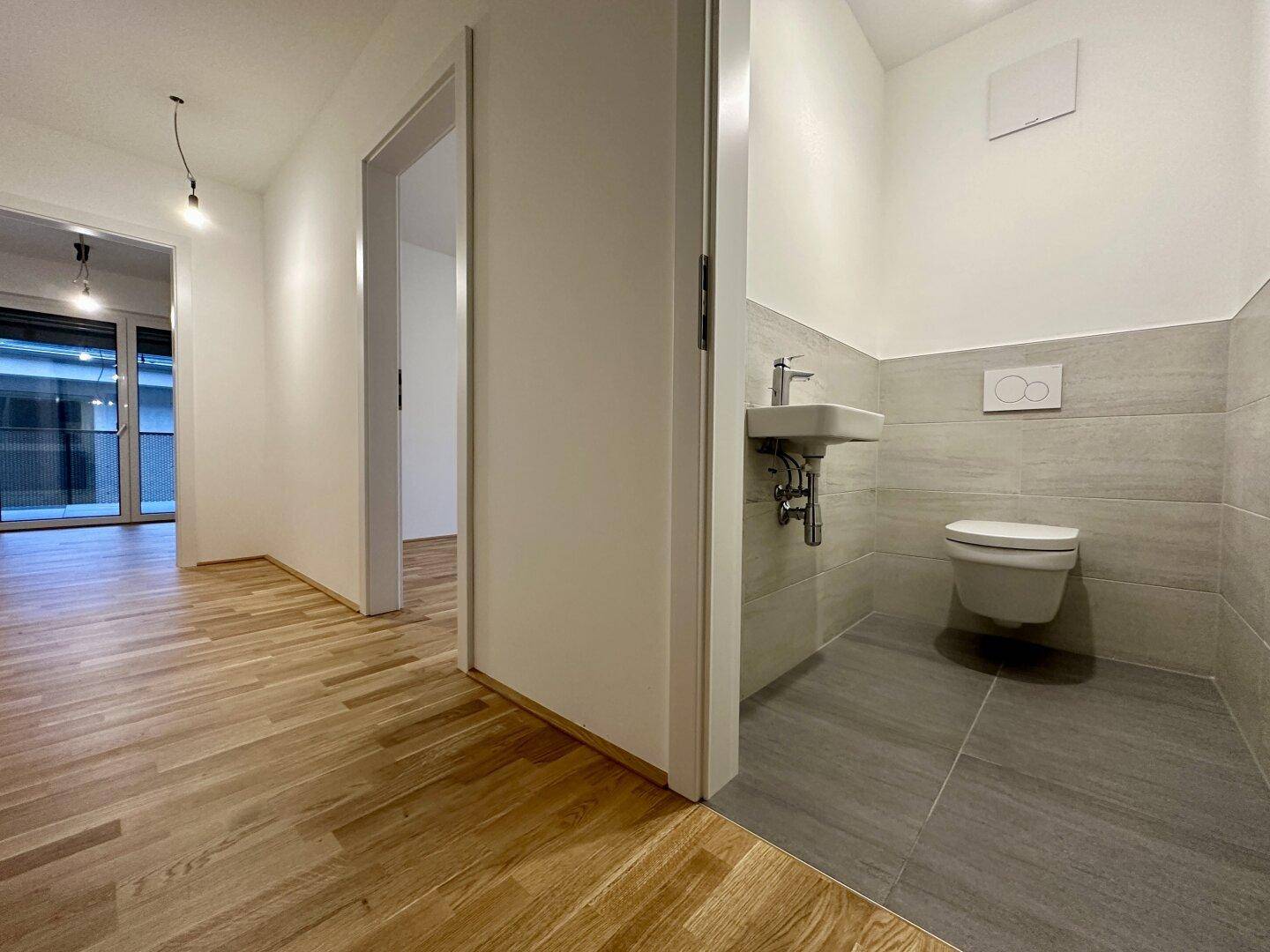 Modernes Gäste-WC mit Wand-WC und kleinem Waschbecken, hell gefliest.