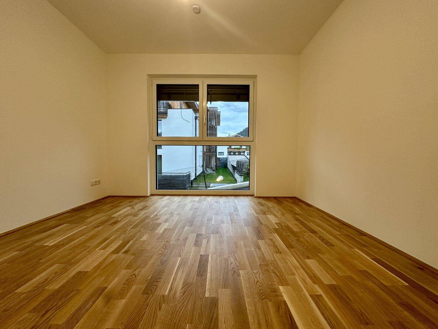 Geräumiges Schlafzimmer mit Parkettboden und großem Fenster mit Blick ins Grüne.