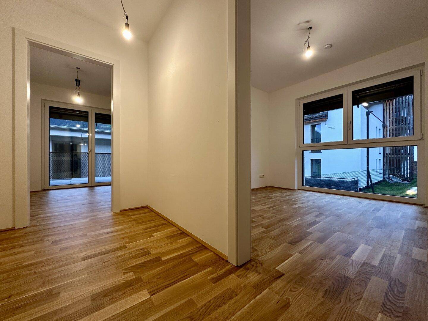 Zwei helle Räume mit Parkettboden und großen Fenstern, die viel Tageslicht bieten.