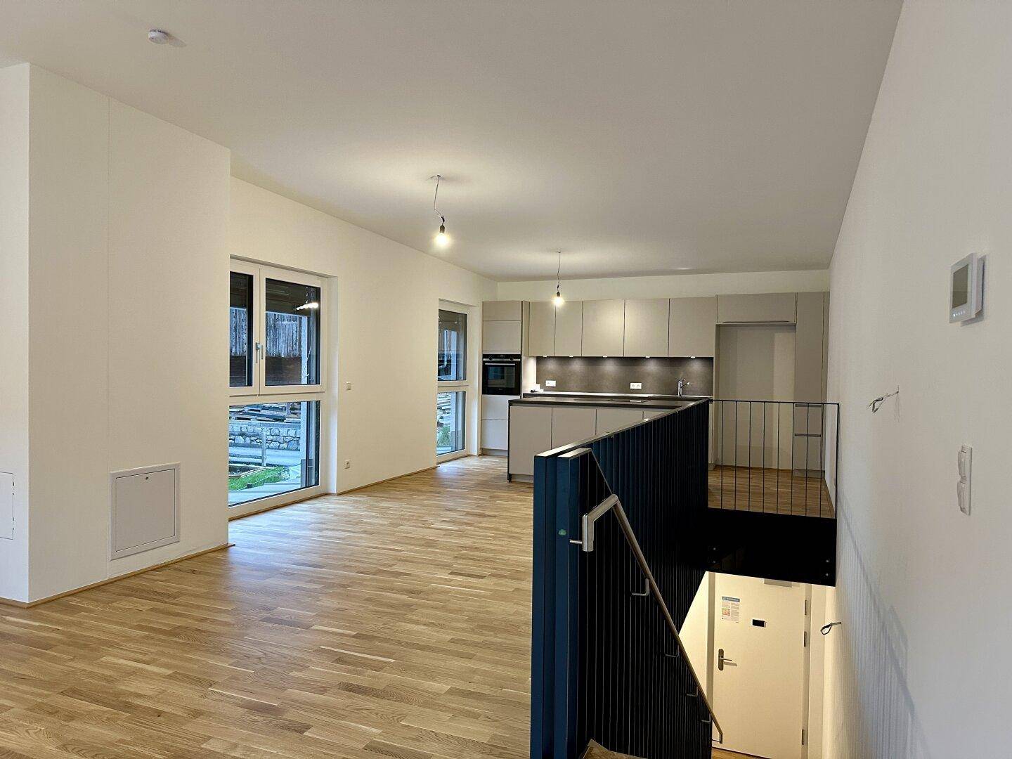 Offener Wohnbereich mit moderner Küche und Treppenabgang, ideal für geselliges Beisammensein.