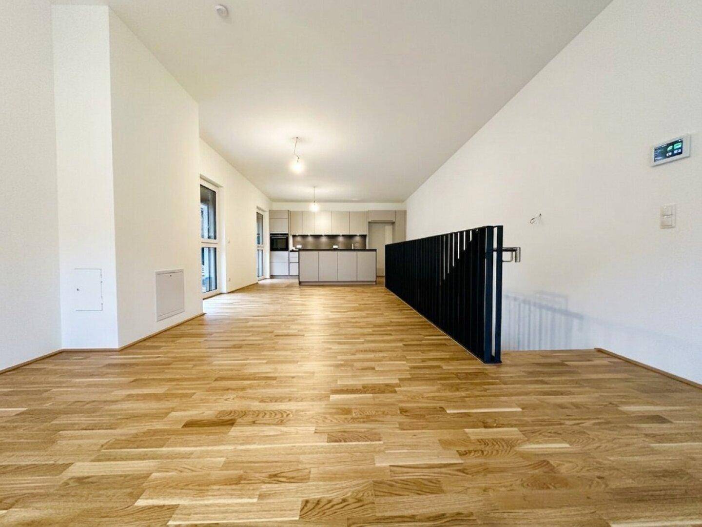 Geräumiger offener Wohnbereich mit Holzboden und Blick auf die moderne Küche.