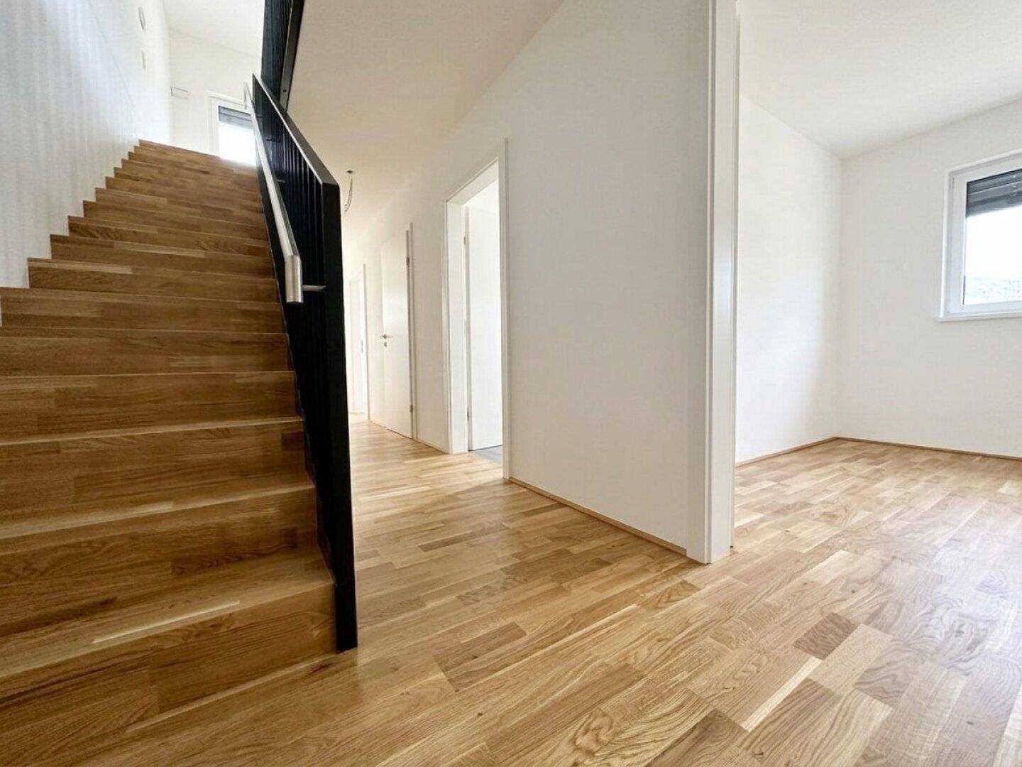 Geräumiger Flur mit Holztreppe und Parkettboden, der zu weiteren Zimmern führt.