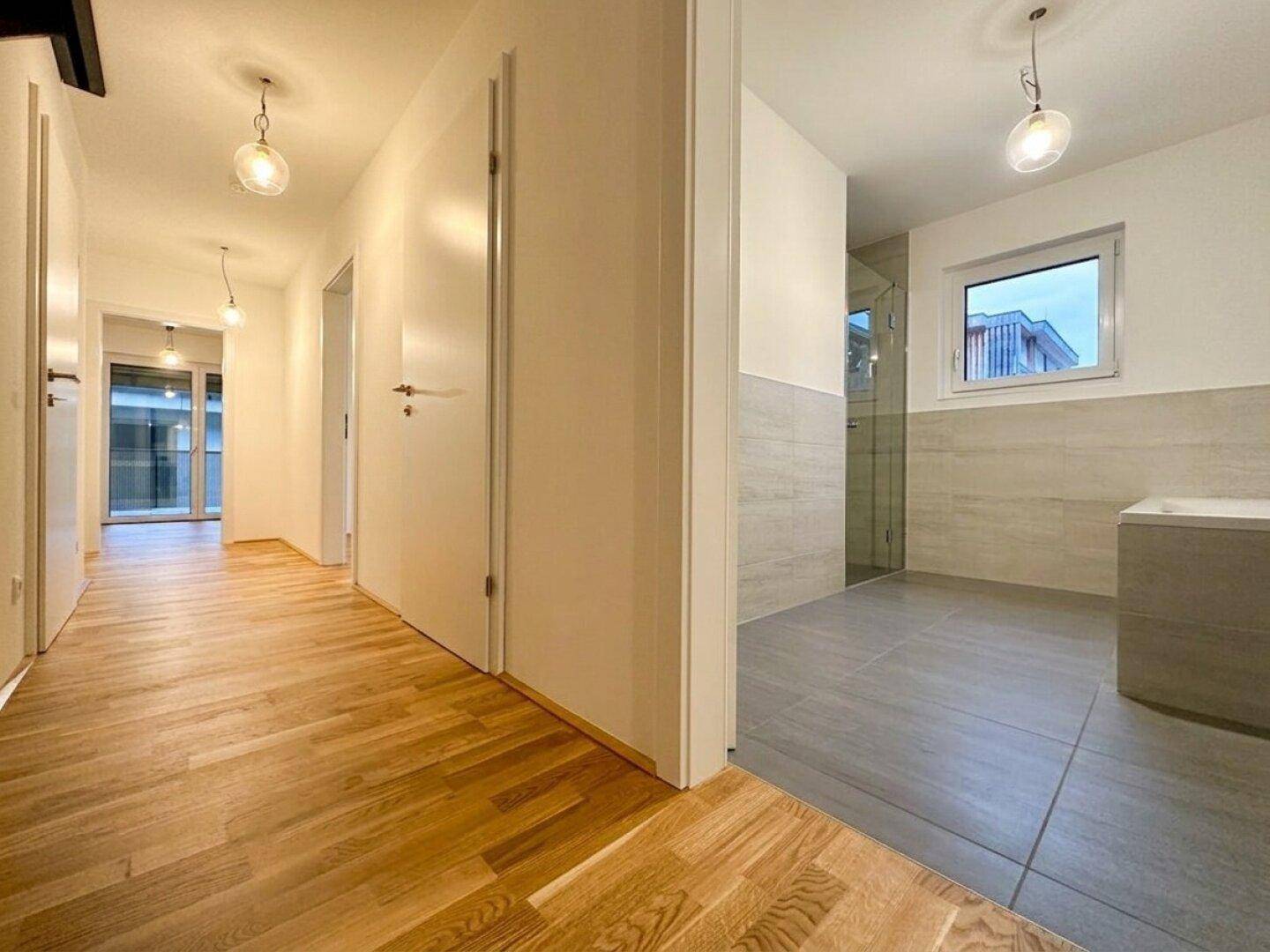 Heller Flur mit Parkettboden und Blick in ein modernes Badezimmer.