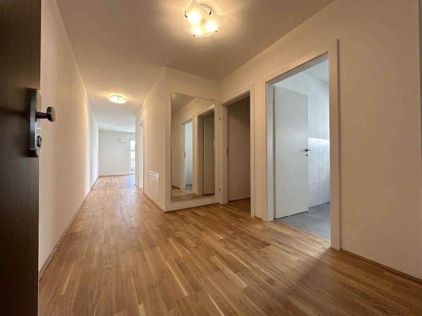 Heller Flur mit Eichenparkettboden und integriertem Spiegel, der zu weiteren Räumen führt.