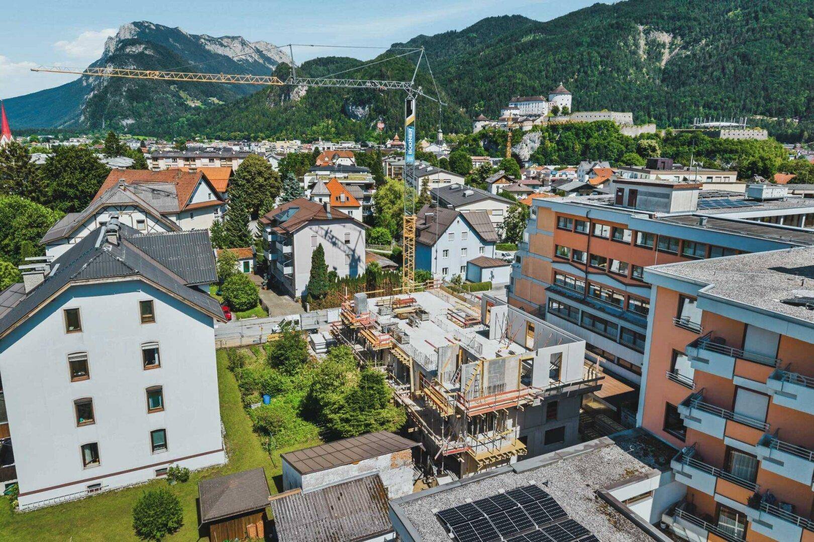 Luftaufnahme einer Baustelle in einer Stadt mit umliegenden Häusern und Bergen im Hintergrund.