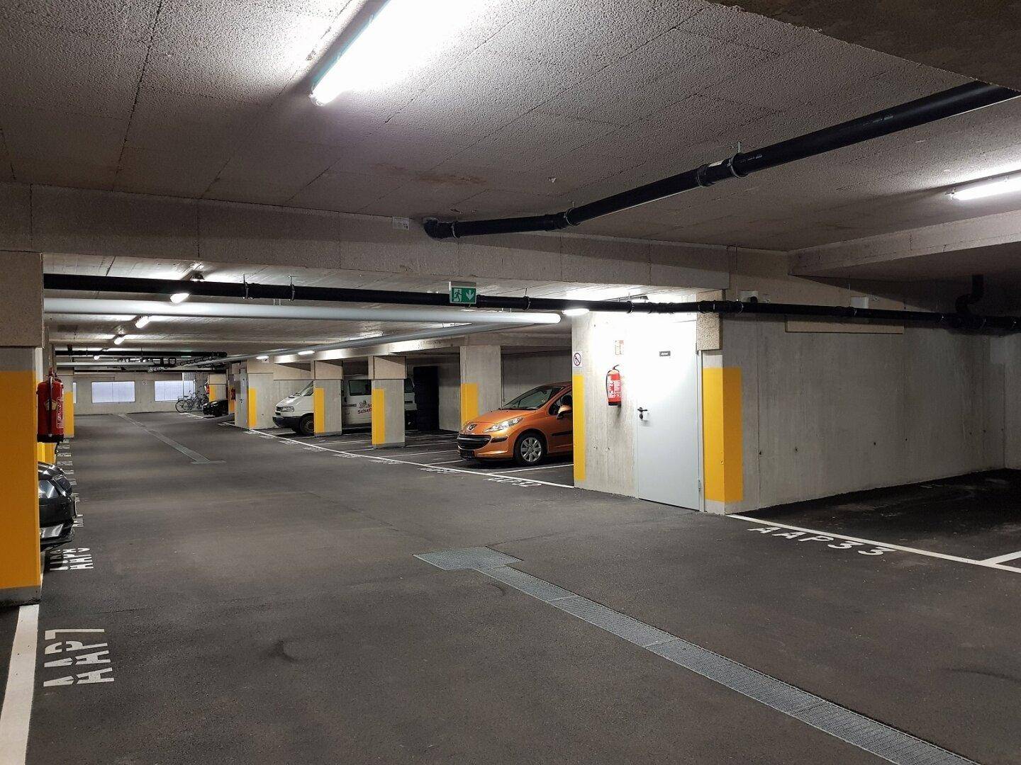 Tiefgarage mit mehreren Stellplätzen, Betonwänden und Decken sowie sichtbaren Installationen.