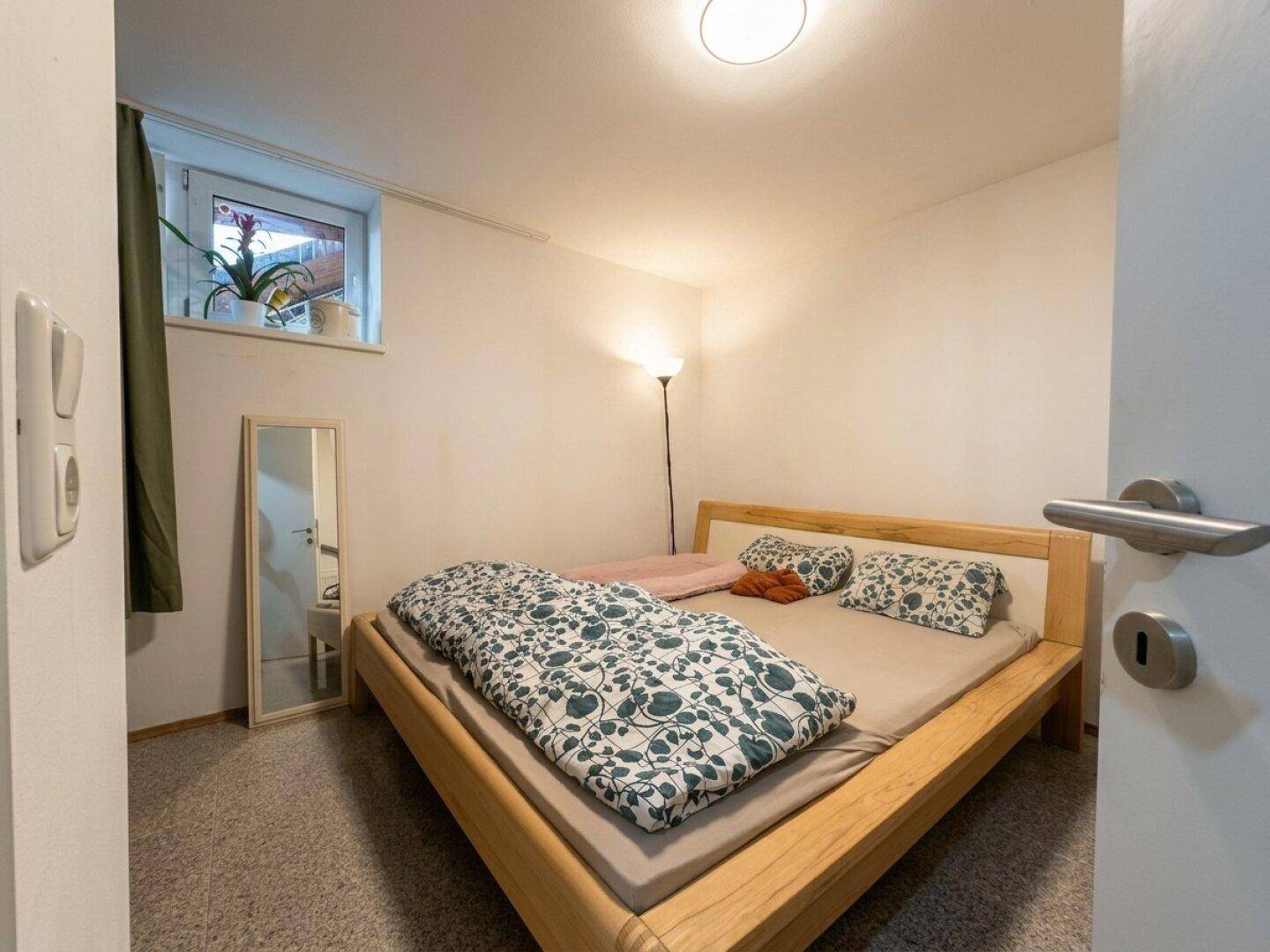 Gemütliches Schlafzimmer mit hellem Holzbett, Teppichboden und kleinem Fenster.