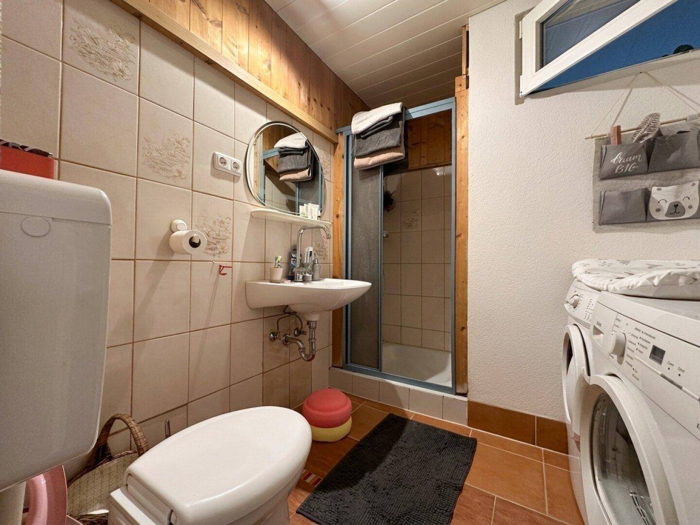 Badezimmer im Landhausstil mit Dusche, WC, Waschbecken und Waschmaschine.
