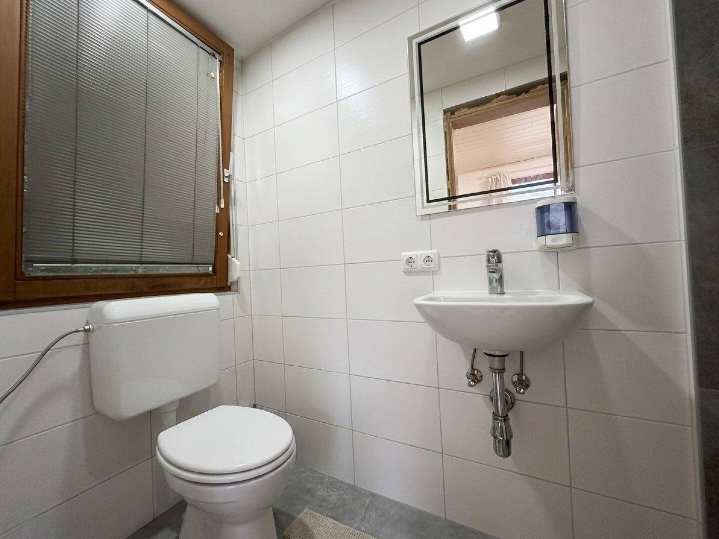 Helles WC mit weißen Fliesen, Fenster und modernem Waschbecken.