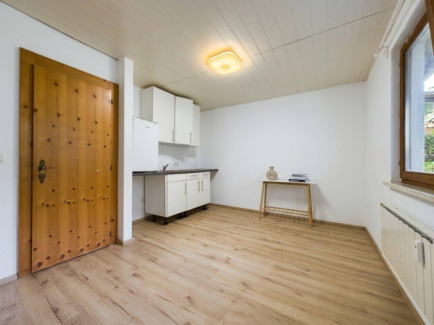 Kleiner Raum mit Laminatboden, einfacher Küchenzeile und Holztür.