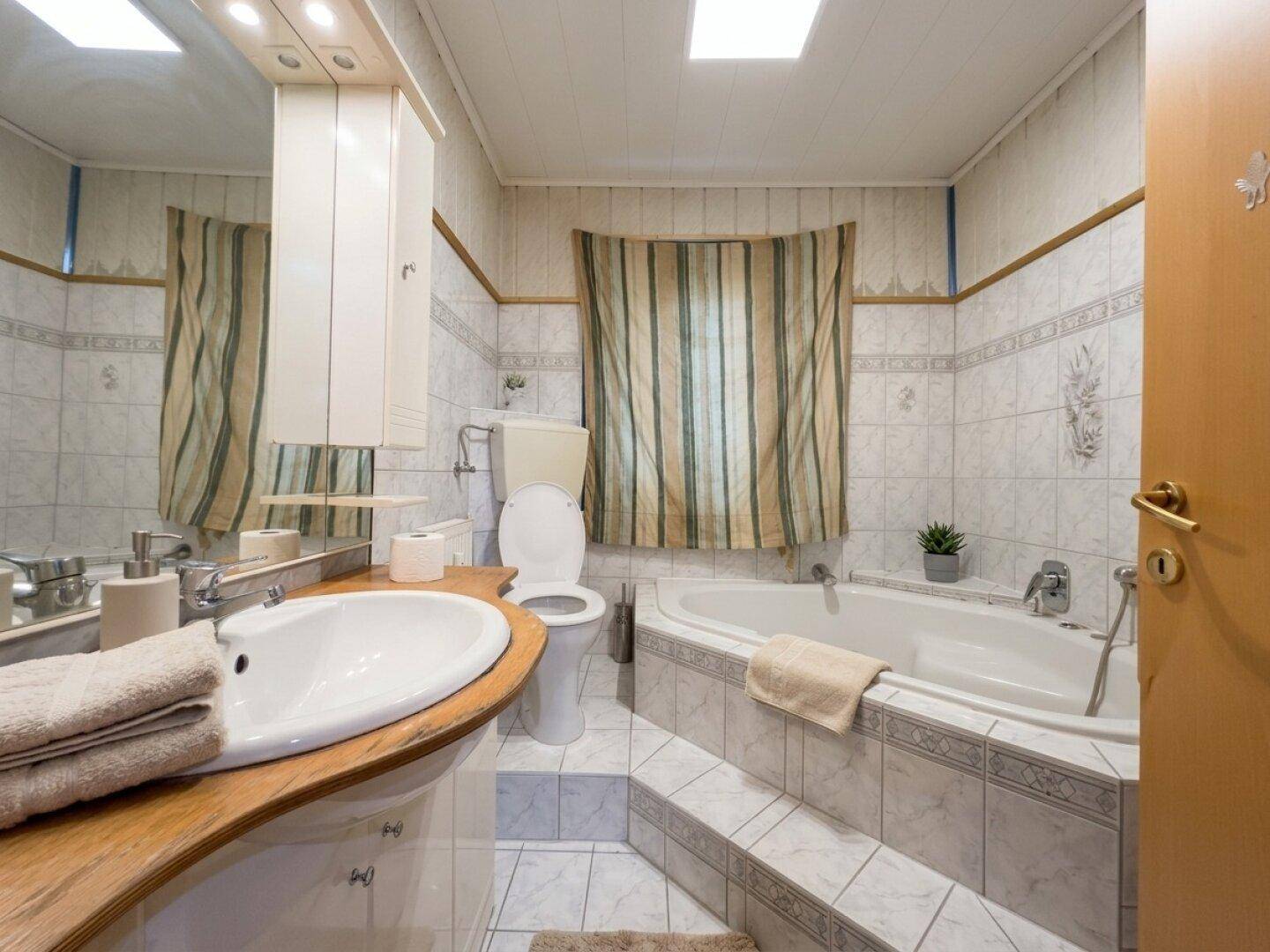 Geräumiges Badezimmer mit Eckbadewanne, WC, Doppelwaschbecken und Fliesenboden.