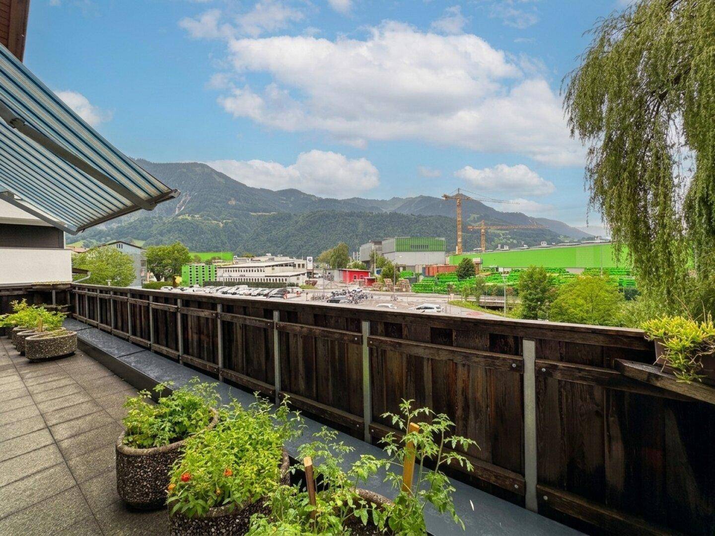 Balkon mit Pflanzen, Holzzaun und Blick auf die umliegende Landschaft und Industrie.