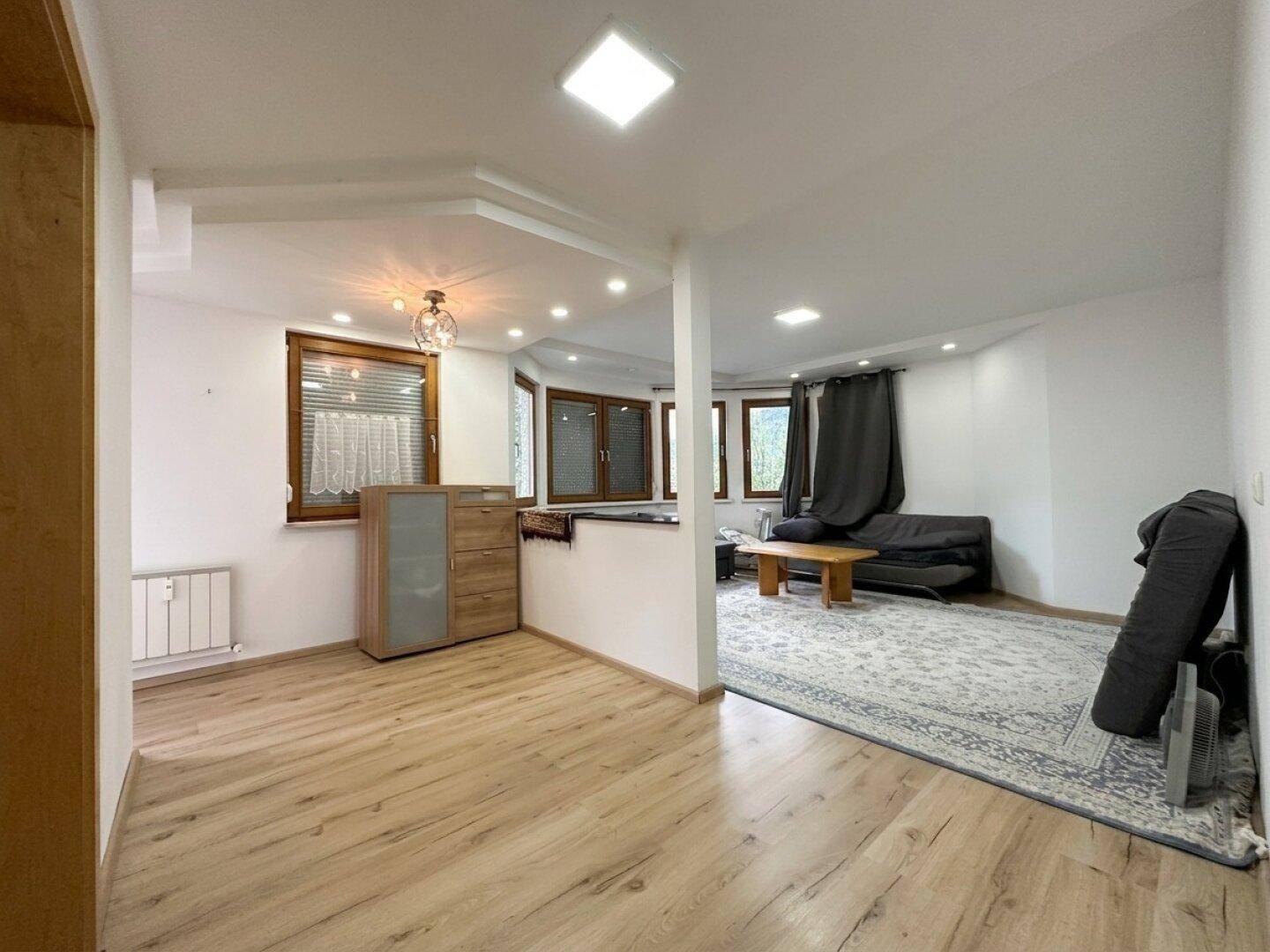 Geräumiger Wohnbereich mit Laminatboden, großen Fenstern und moderner Einrichtung.