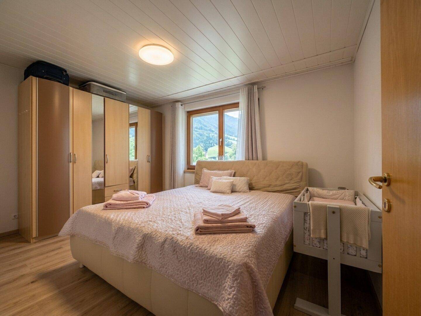 Helles Schlafzimmer mit Doppelbett, Kleiderschrank und Blick auf die Berge.