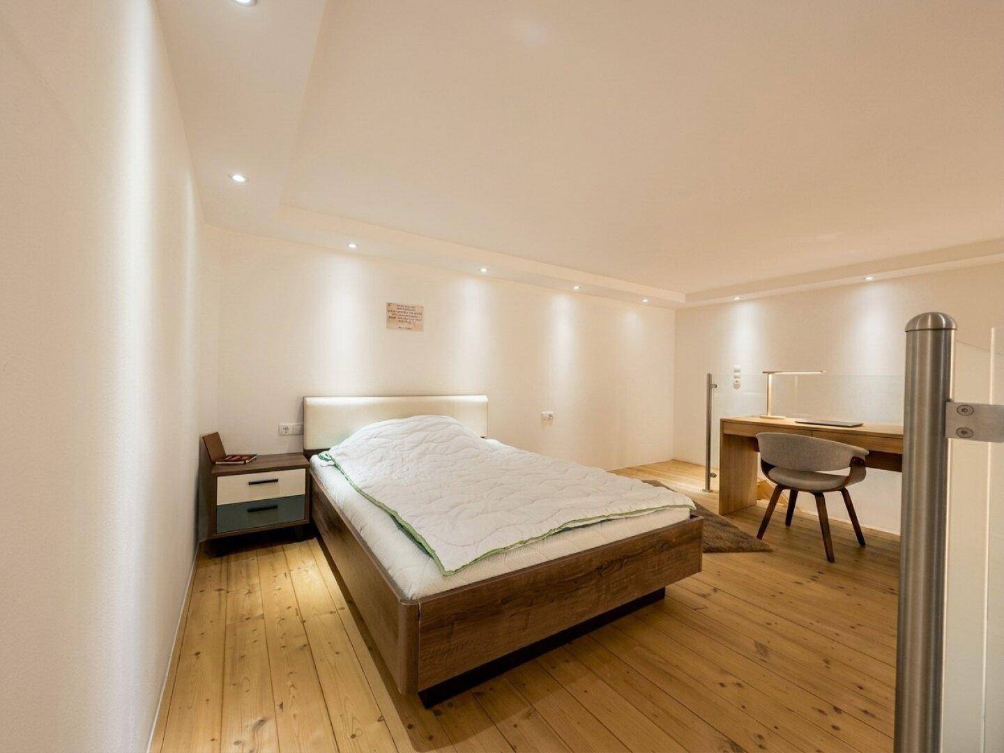 Helles Schlafzimmer mit Holzboden, Einzelbett und Schreibtischbereich.