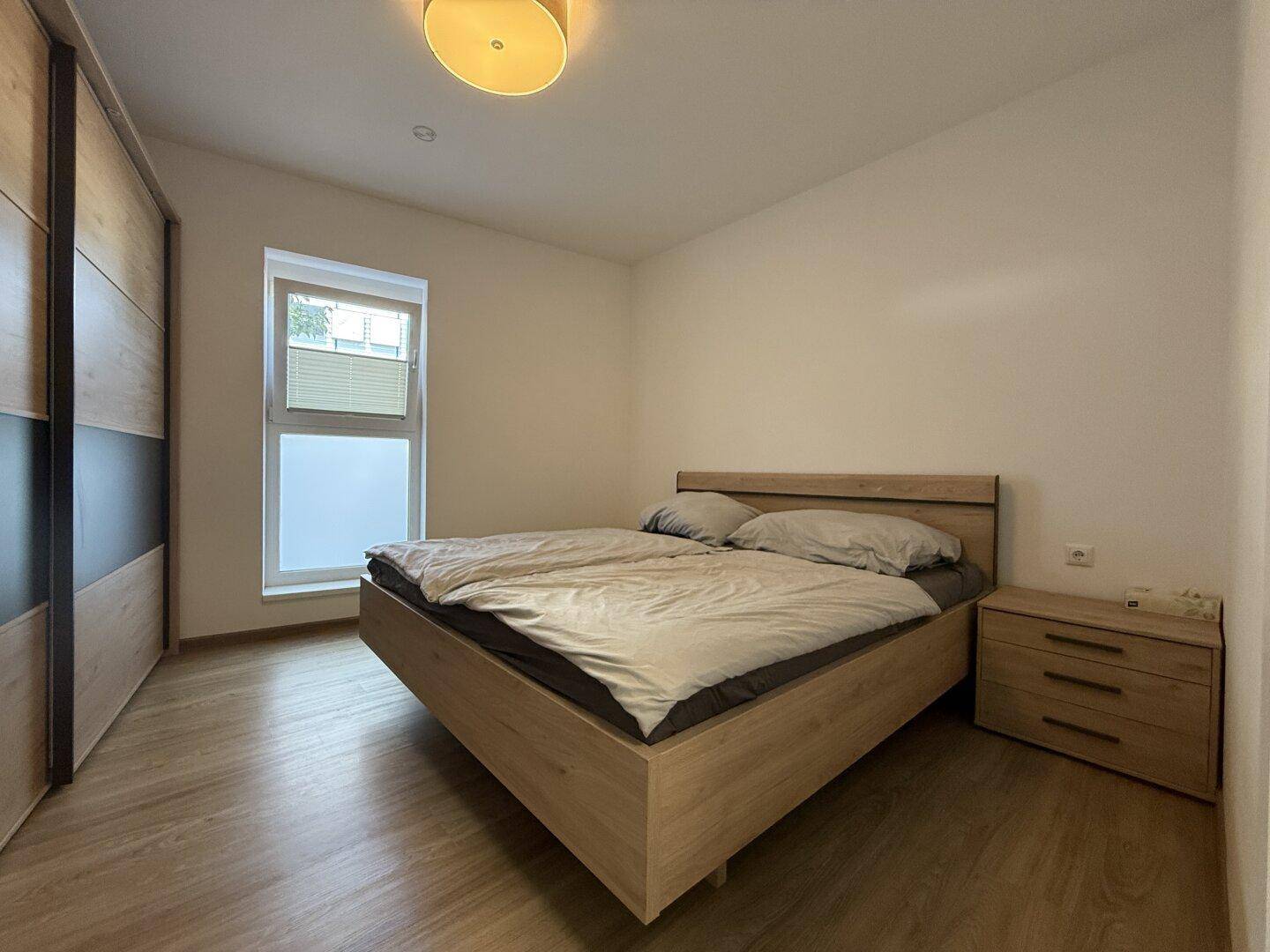 Gemütliches Schlafzimmer mit modernem Holzbett, passendem Nachttisch und großem Kleiderschrank.