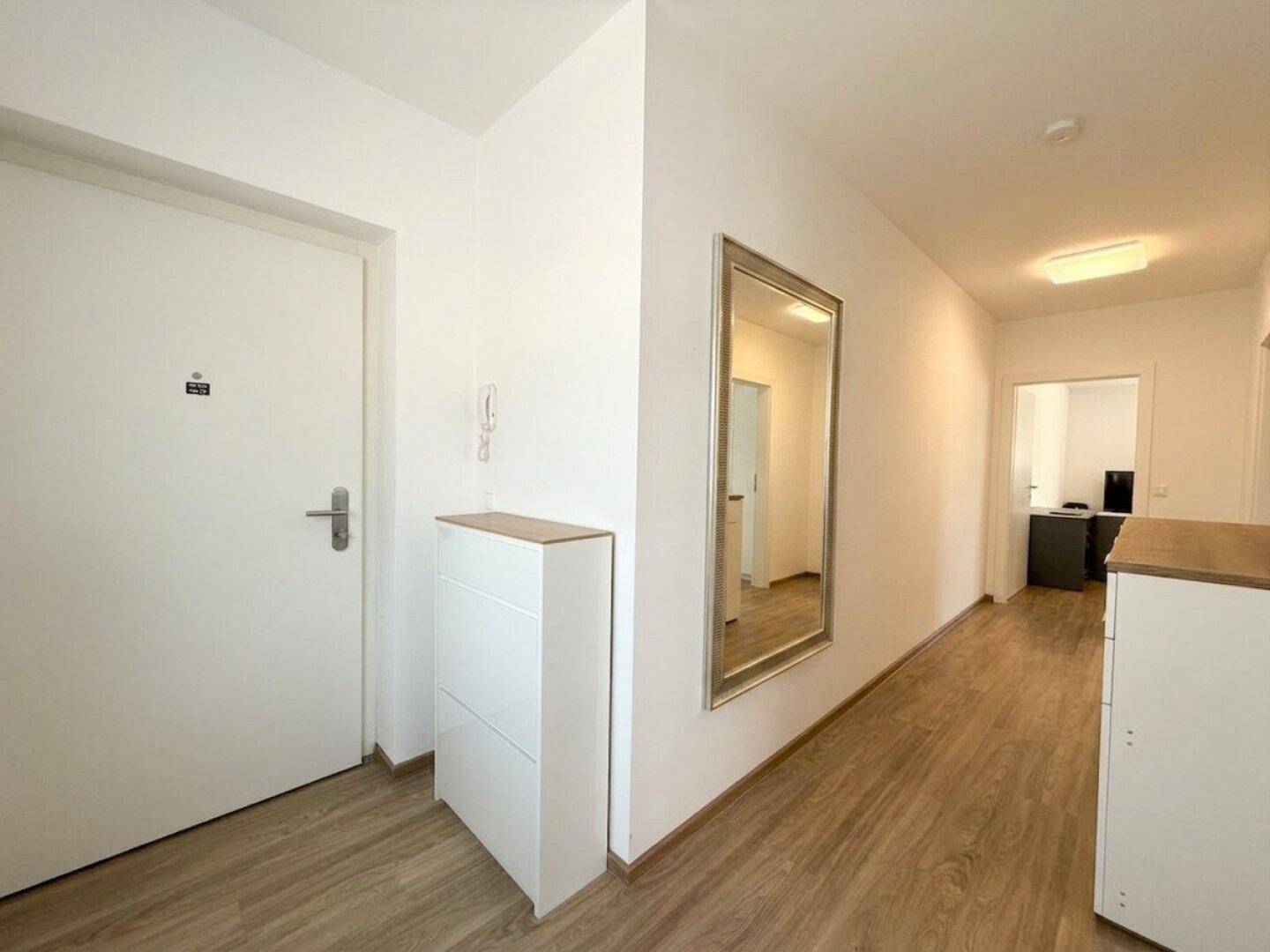 Heller Eingangsbereich mit Holzoptikboden, weißer Tür und einem großen Wandspiegel.