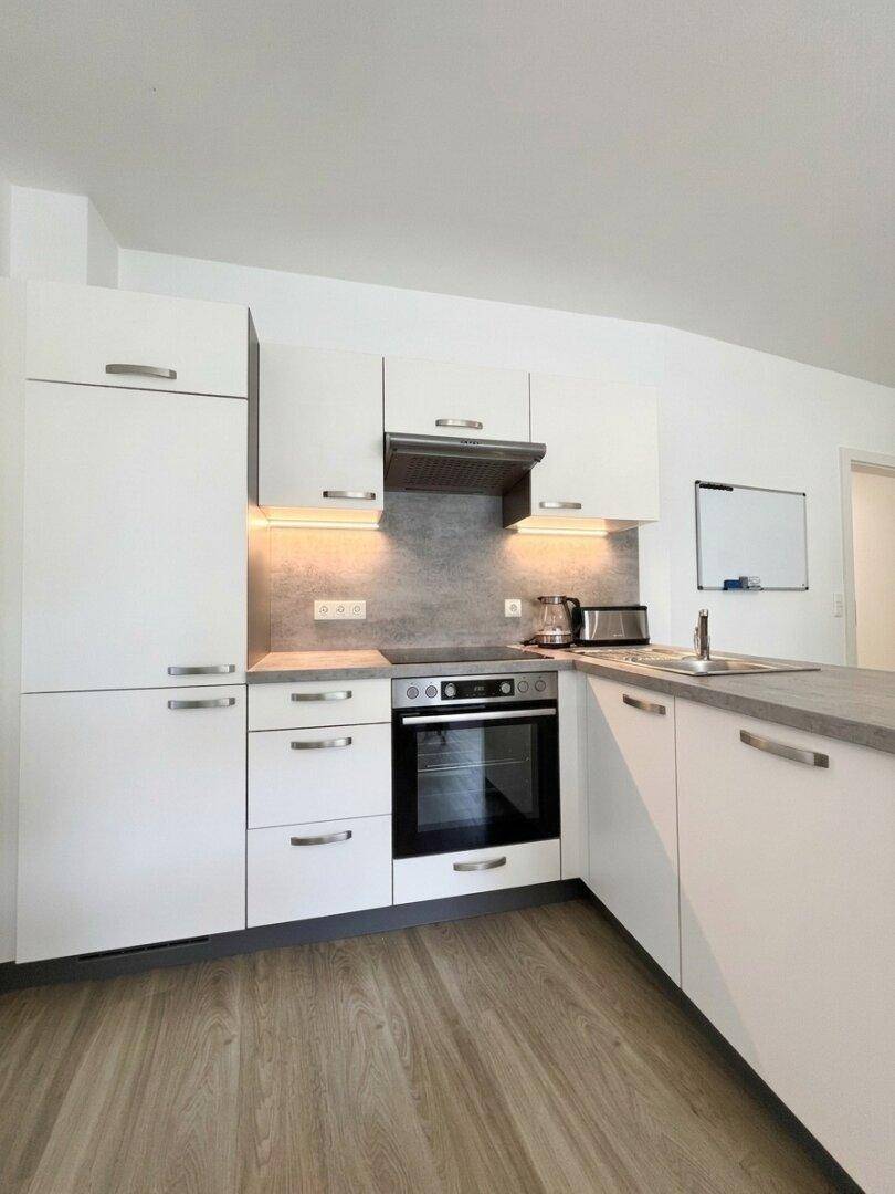 Moderne Einbauküche mit weißen Schränken, integriertem Backofen und Dunstabzugshaube.
