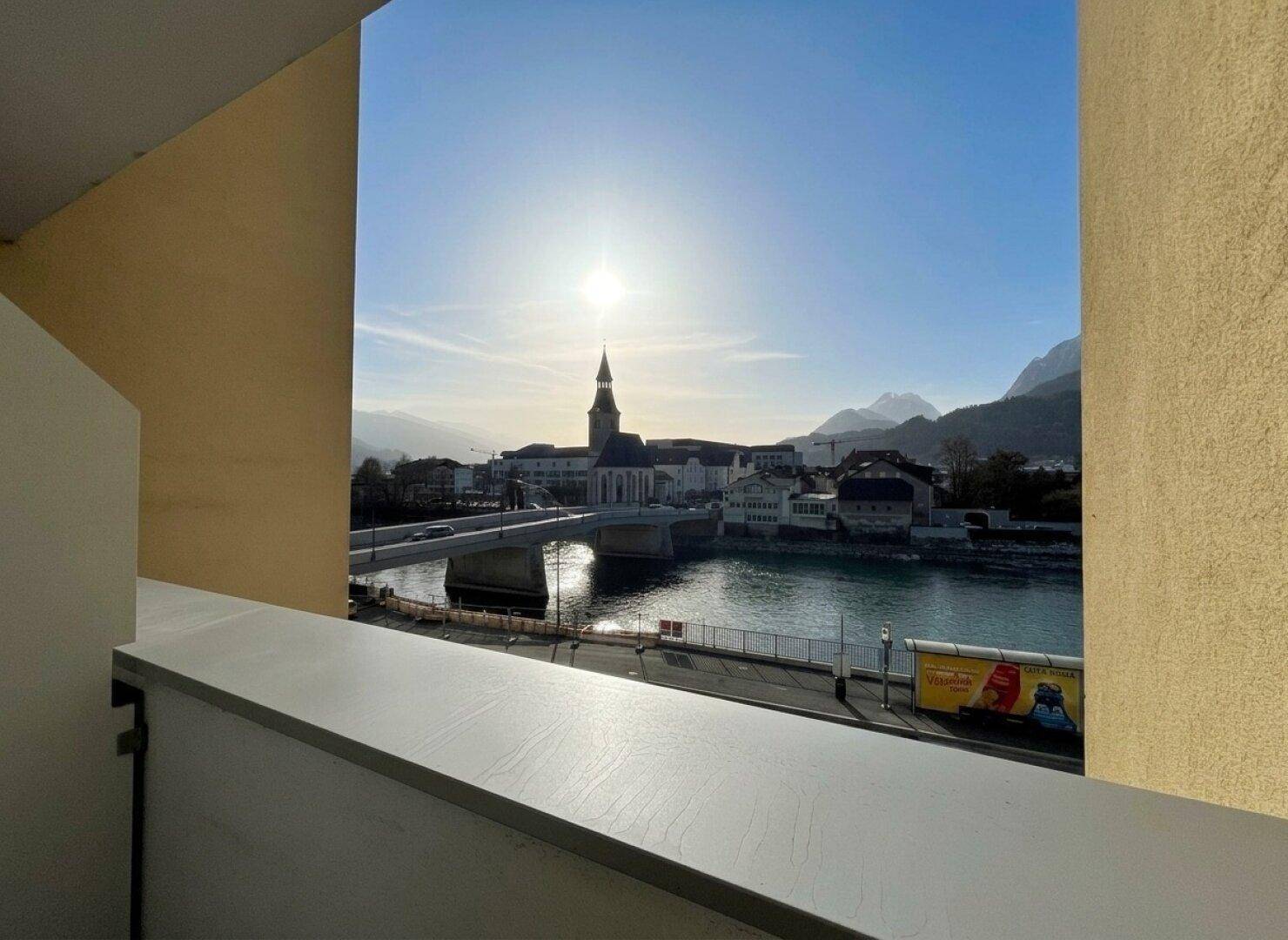 Sonniger Ausblick vom Balkon auf Fluss, Brücke, Kirche und die umliegende Berglandschaft.