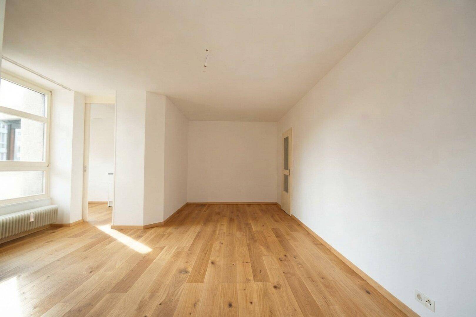 Geräumiges, helles Zimmer mit Holzboden und weiß gestrichenen Wänden, bereit zur Einrichtung.
