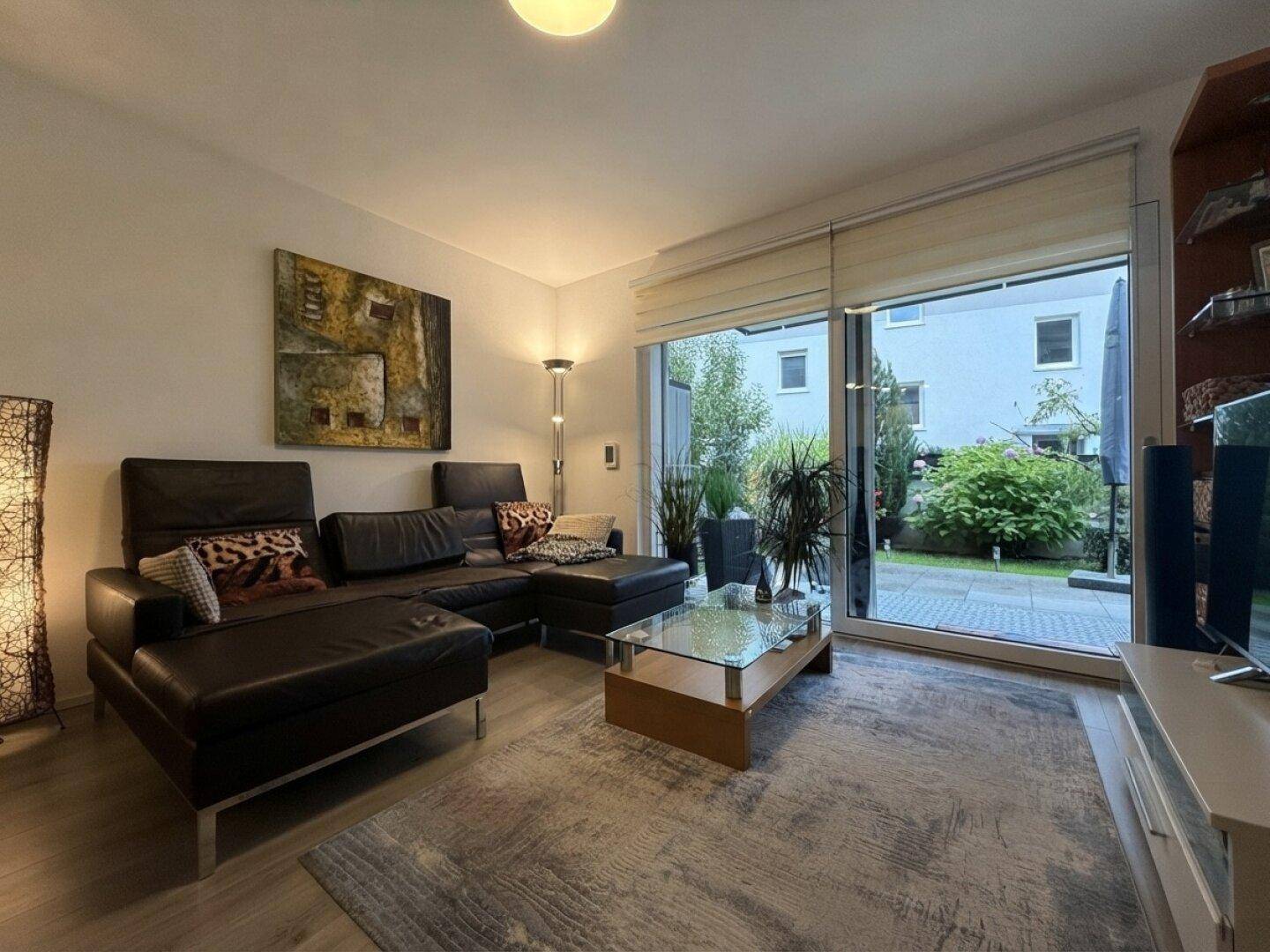 Modernes Wohnzimmer mit Ledersofa, Couchtisch und großen Fenstern zum Garten.