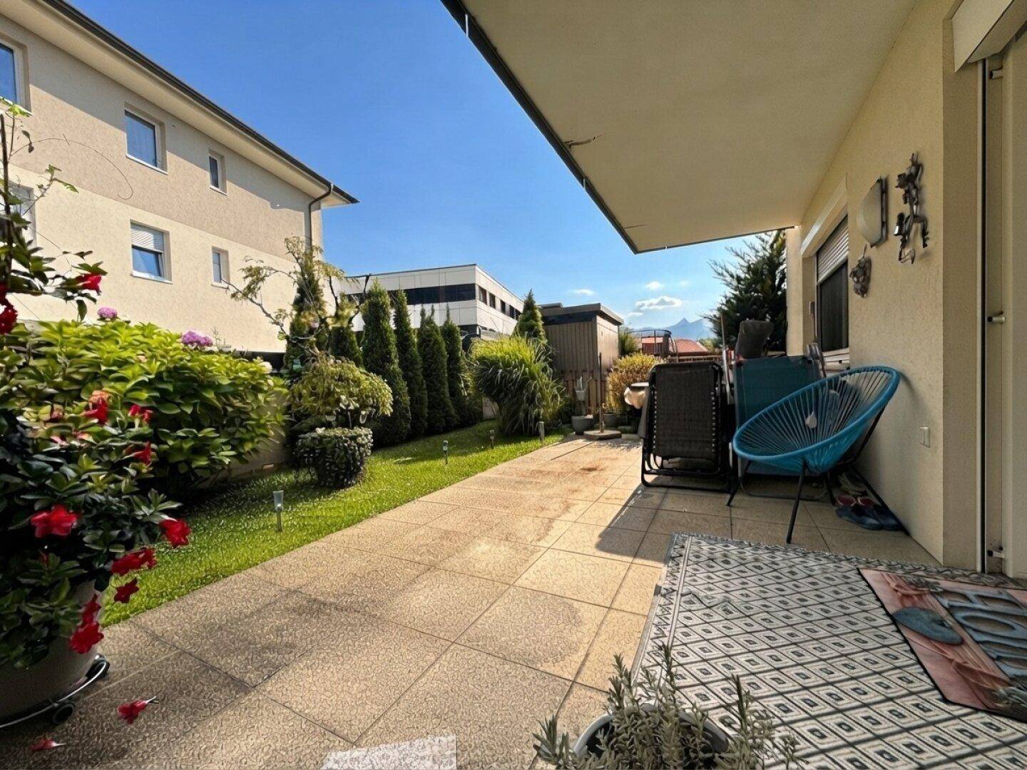 Sonniger Außenbereich mit gepflasterter Terrasse, Gartenmöbeln und gepflegter Grünfläche.