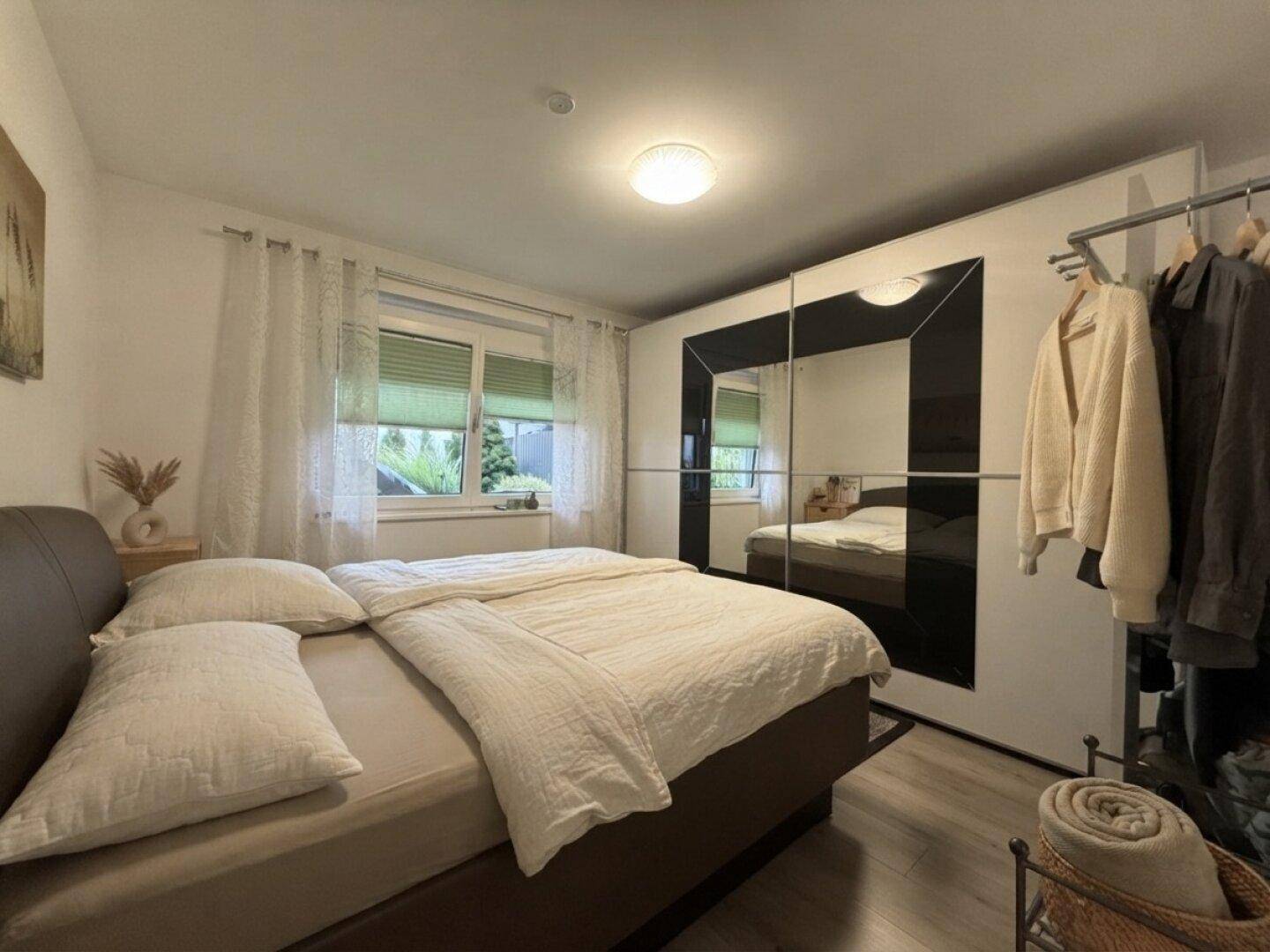Schlafzimmer mit Doppelbett, Spiegelschrank und Blick ins Grüne durch das Fenster.
