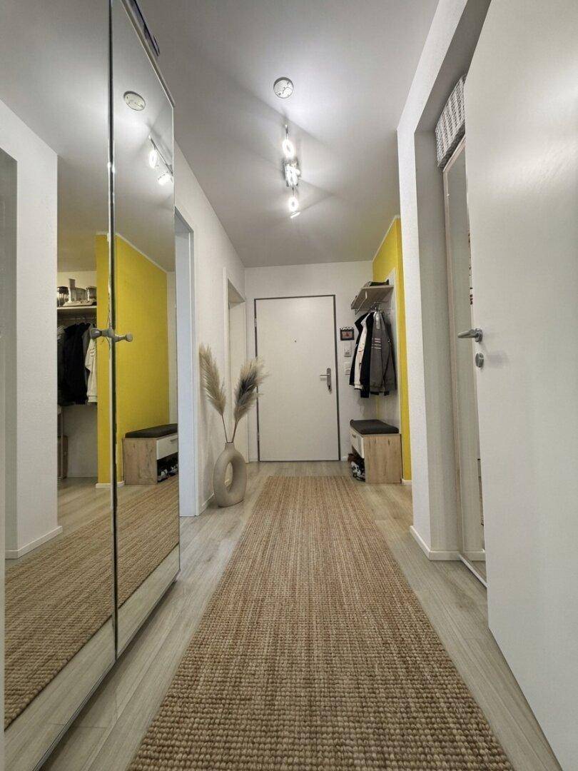 Heller Flur mit Spiegelschrank, Holzboden und gelb gestrichener Akzentwand.