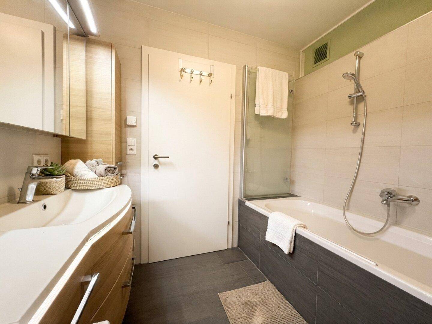 Modernes Badezimmer mit Badewanne, Duschabtrennung und elegantem Waschtisch mit Unterschrank.