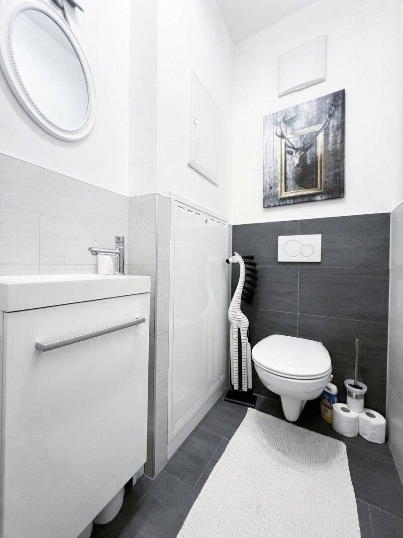 Kleines Gäste-WC mit modernem Wand-WC, Waschbecken und dunklen Fliesen.