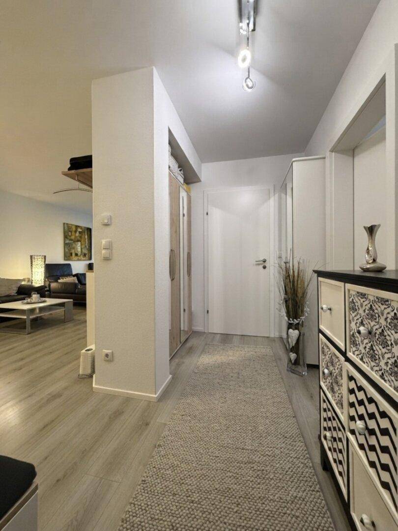 Eingangsbereich mit Garderobe, Kommode und hellem Laminatboden, offen zum Wohnbereich.