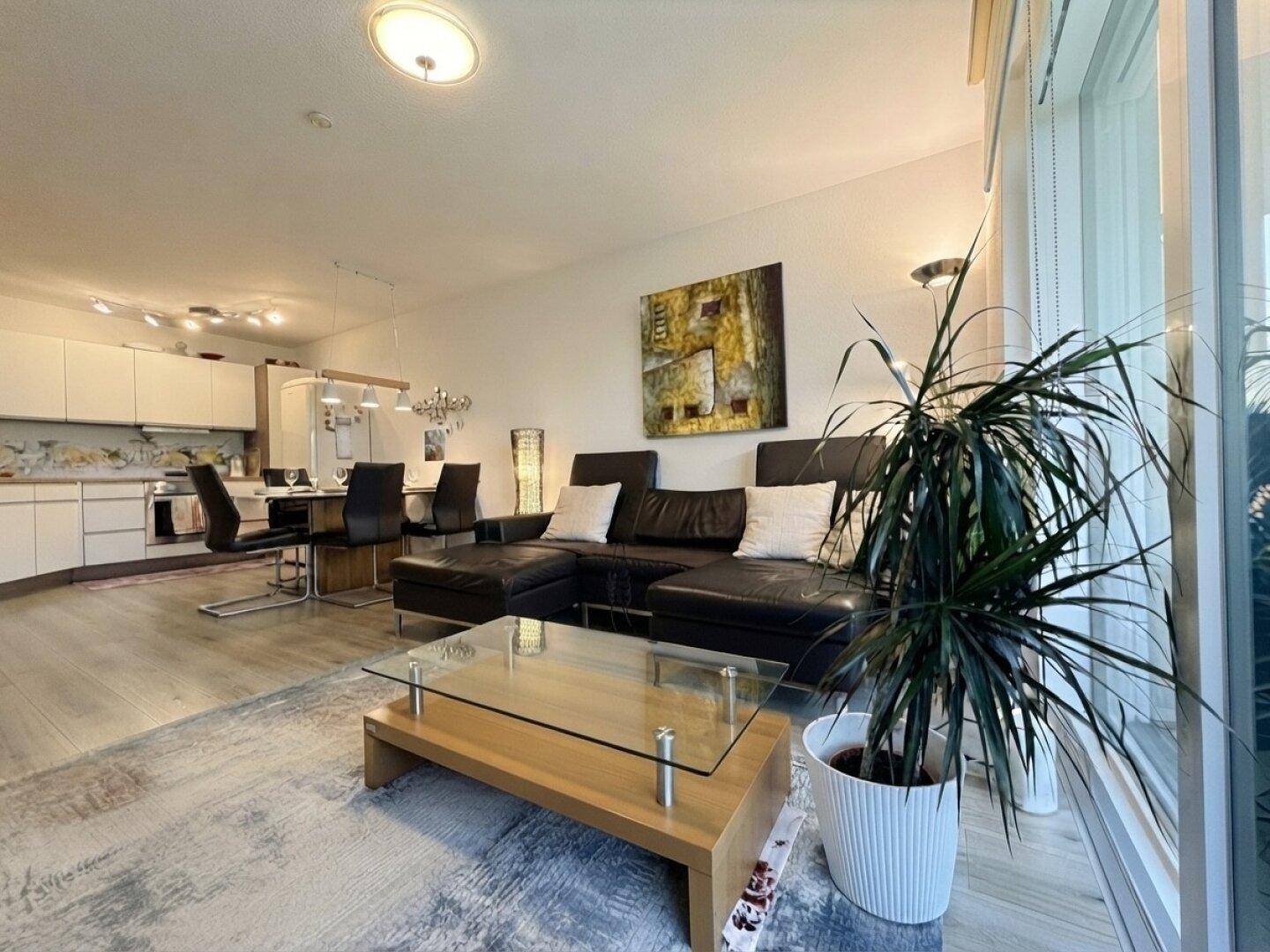 Heller offener Wohn- und Essbereich mit moderner Küche, Ledersofa und großem Fenster.
