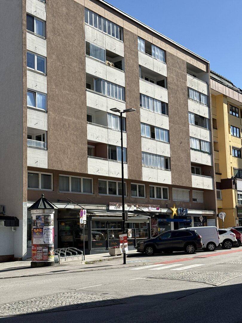Nahaufnahme der Fassade eines mehrstöckigen Wohngebäudes mit Balkonen und Geschäften im Erdgeschoss.