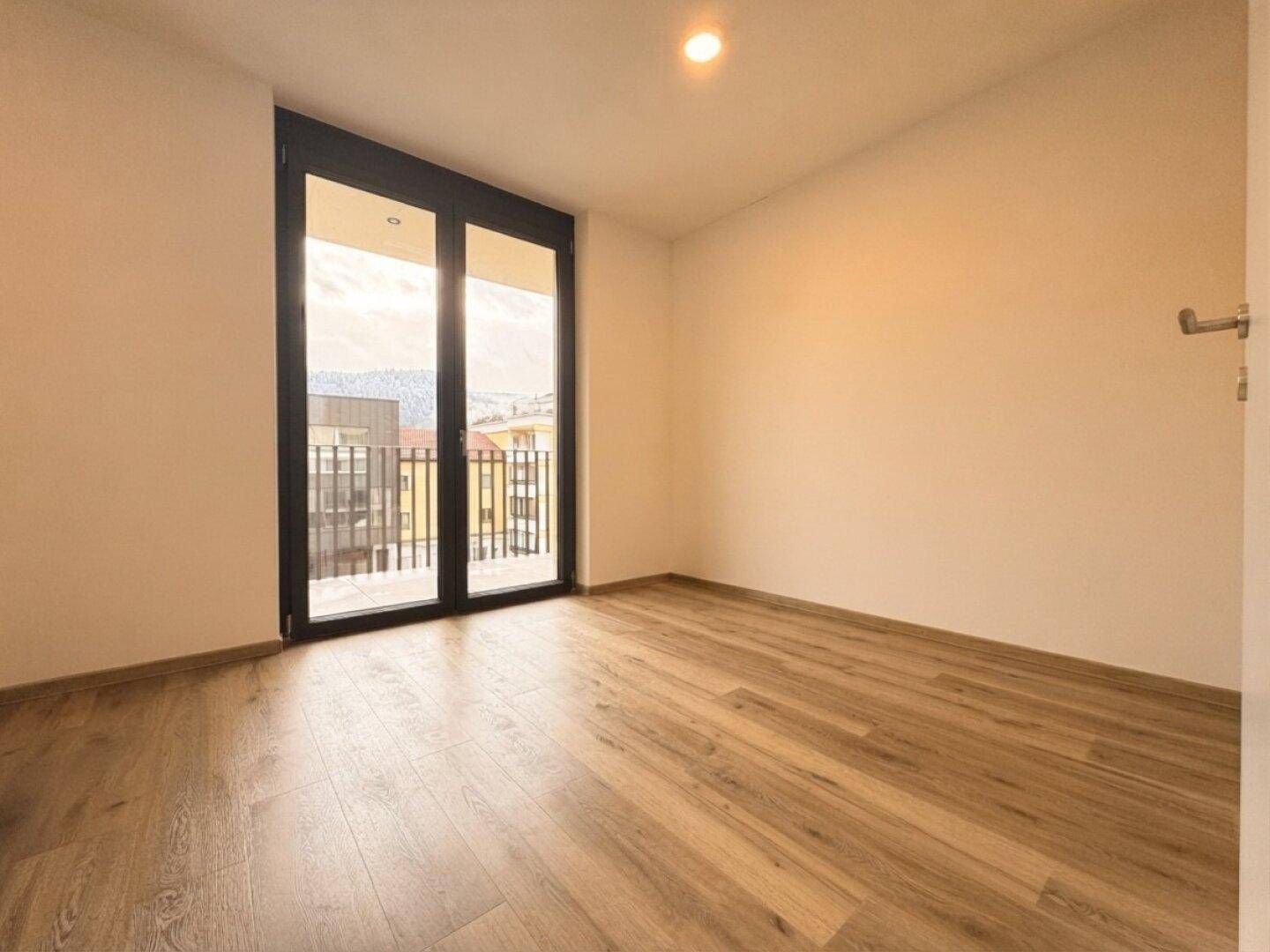 Helles Zimmer mit Holzboden und Zugang zu einem französischen Balkon, mit Blick auf die Umgebung.