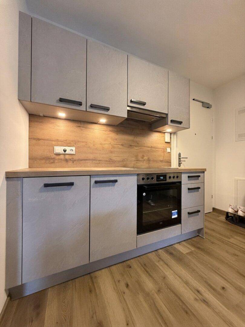 Moderne Einbauküche mit grauen Schränken, Holzarbeitsplatte und integriertem Backofen.