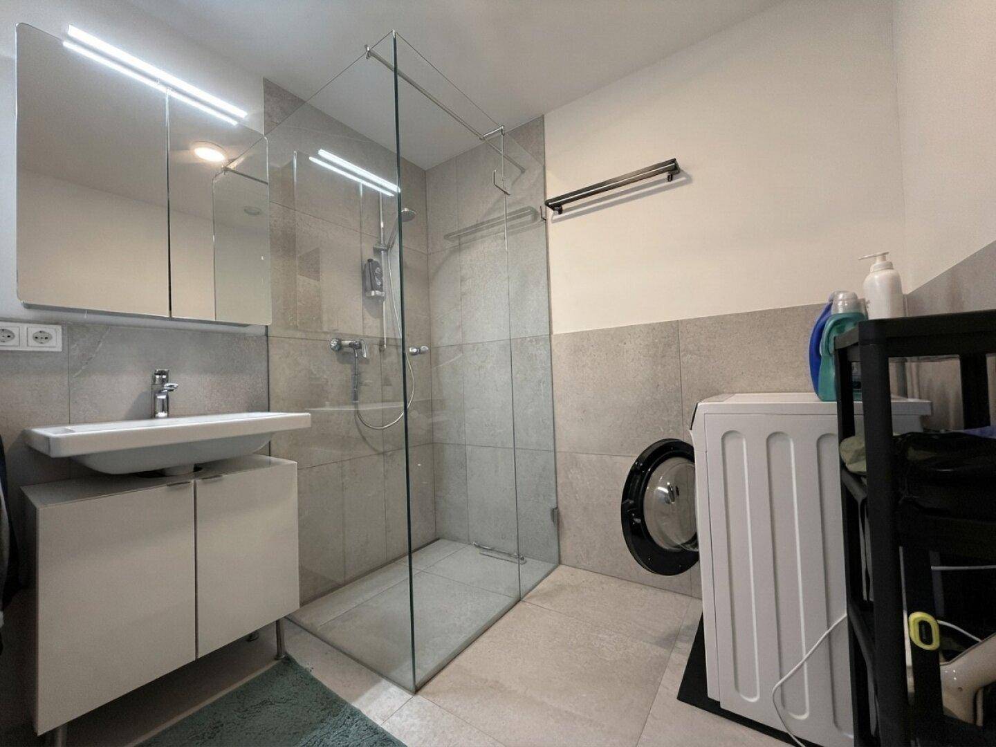 Modernes Badezimmer mit begehbarer Dusche, Waschbecken und Waschmaschine.