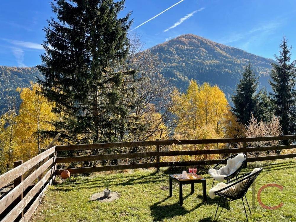 Gemütlicher Sitzbereich im Garten mit Blick auf die beeindruckende Berglandschaft und Herbstbäume.