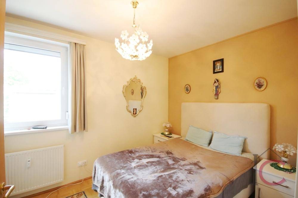 Gemütliches Schlafzimmer mit hellem Bett, Fenster und dekorativem Spiegel.