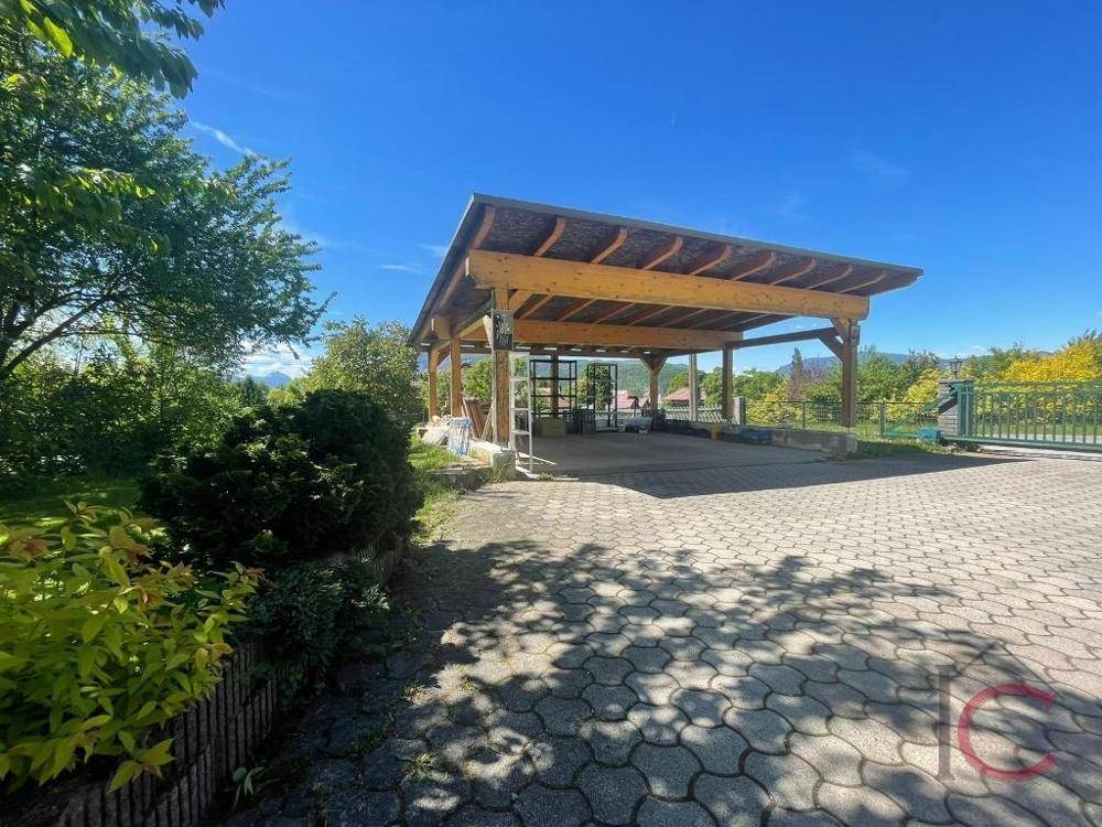 Geräumiger Holzcarport mit breiter Zufahrt und üppiger Bepflanzung im sonnigen Außenbereich.