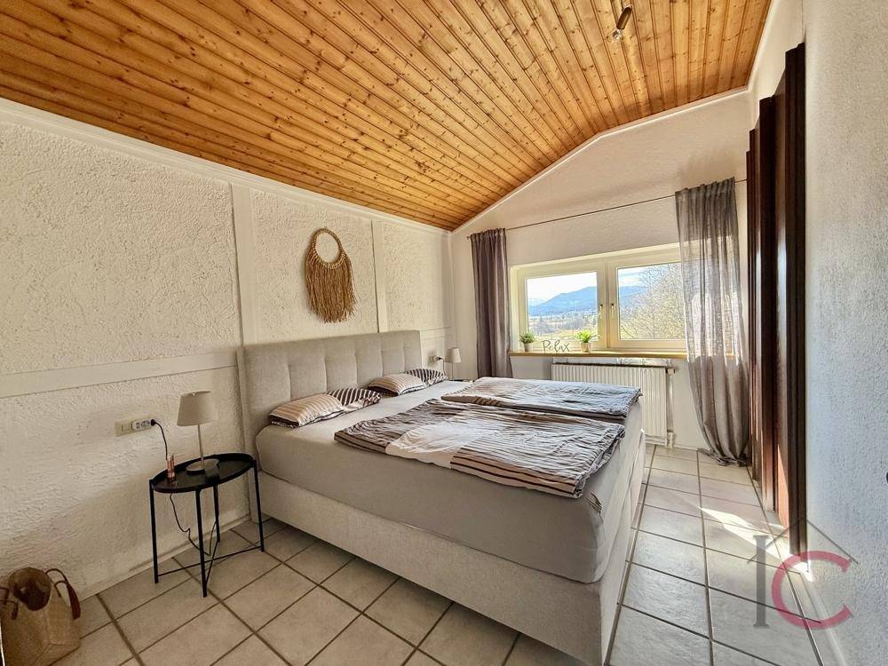 Gemütliches Schlafzimmer mit Doppelbett, Holzdecke und Fenster mit Bergblick.